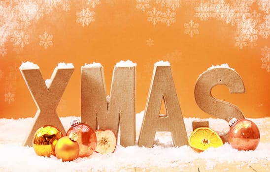 Colorful Xmas background with falling snowflakes and wooden letters spelling Xmas covered in snow with orange and gold decorations and fruit on a warm toned orange background