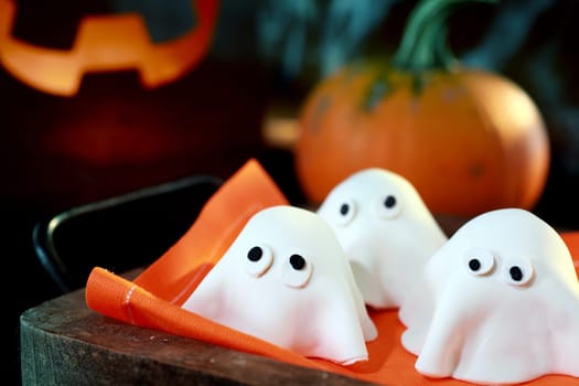 Tray of cute little Halloween monsters or ghosts made of pastry dough for a delicious party snack with a fresh pumpkin and glowing jack-o-lantern behind