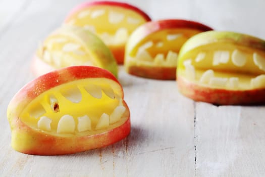 Creative homemade healthy snacks for Halloween made of carved apples shaped like scary open mouths, on a wooden table
