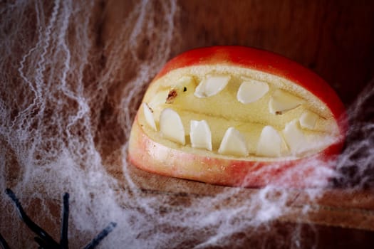 Ghoulish gaping Halloween mouth with teeth made from an apple on a wooden shelf festooned with spider webs in a scary festive background for Allhallows Eve