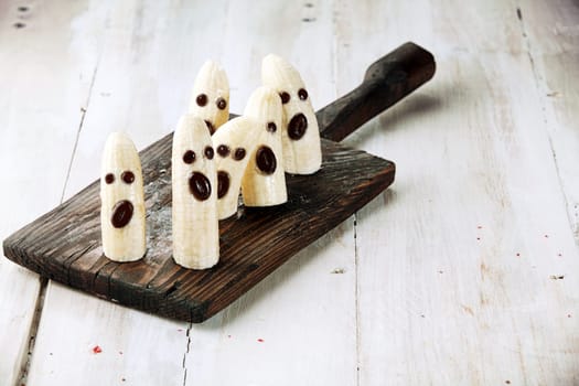 Banana Halloween Ghosts with Chocolate Faces on Wooden Cutting Board