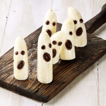 Banana Halloween Ghosts with Chocolate Faces on Wooden Cutting Board