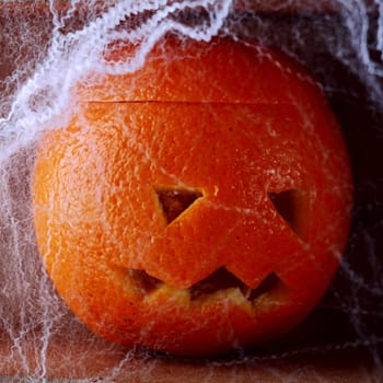 Colorful fresh orange Halloween lantern carved with a traditional jack-o-lantern face covered in spooky eerie cobwebs for a creative rustic handicraft Halloween background