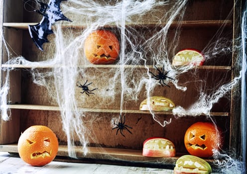 Spooky Halloween pantry with pumpkin lanterns and apples shaped as open mouths with teeth on wooden shelves draped in spider webs crawling with large black spiders