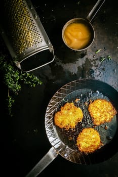 Delicious fresh fried potato fritters made from grated potato, fresh herbs and egg in a country kitchen with a vintage grater, view from overhead with ingredients