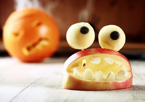 Cute homemade Halloween apple decoration of an open mouth with teeth topped with googly dough eyes on toothpicks for a scary but healthy favor to give children trick-or-treating
