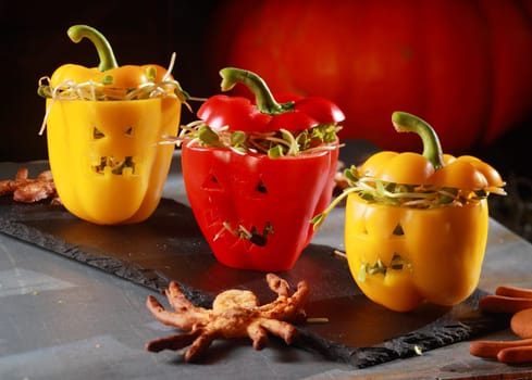 Halloween themed salad with stuffed red and yellow sweet peppers with cutout faces like jack-o-lanterns served with a flying bat pastry on a curved bark plate