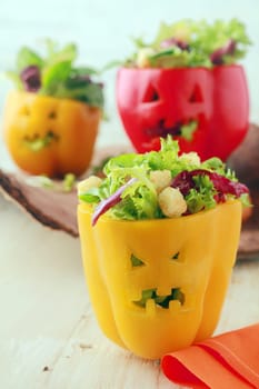 Colorful Halloween food background with creative stuffed red and yellow sweet bell peppers with faces cut into the skin like Halloween pumpkin lanterns filled with fresh green salad and cheese