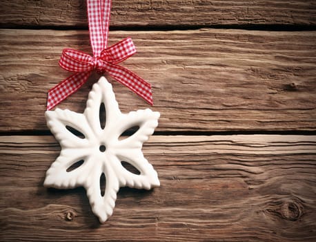 White Christmas snowflake decoration hanging from a fresh red and white ribbon and bow on rustic weathered wooden boards with copyspace for your festive greeting