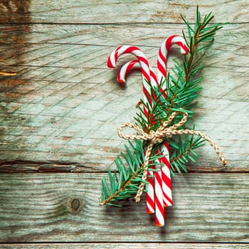 Colorful striped red and white Christmas candy canes tied in a bundle with sprigs of pine with string on a rustic wooden background, square format with copyspace