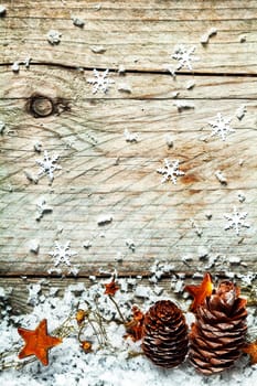 Christmas country background with a garland of decorative golden orange stars draped over pine cones in snow below a textured wooden background with snowflake decorations and copyspace