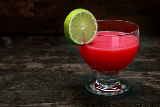 Bloody Mary tomato cocktail garnished with lemon standing on an old wooden bar counter against a dark background with copyspace