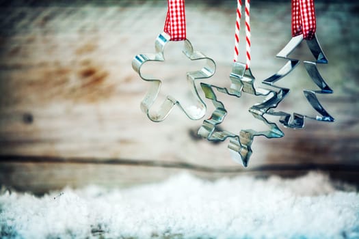 Rustic Xmas cookie cutters hanging from red and white ribbons above winter snow against an old wooden background with copyspace