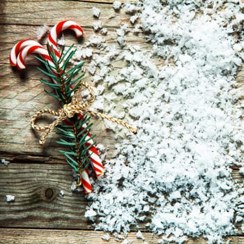 Bundle of striped red and white Christmas candy canes tied with string in scattered snow on rustic wooden boards