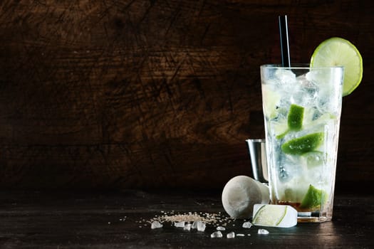 Refreshing Christmas cocktail with a blend of white spirits, mixer and fresh aromatic herbs in a tall glass with ice garnished with tangy lemon, dark background with copyspace
