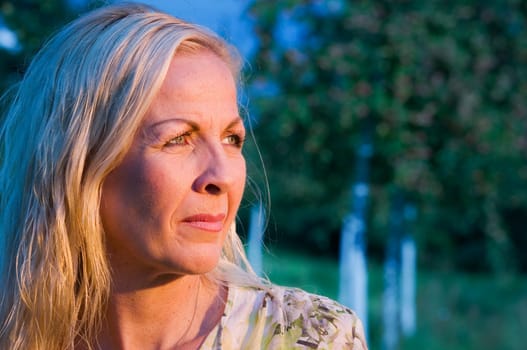 Side head-and-shoulder portrait of a middle-aged blonde woman in a park looking into the sunset