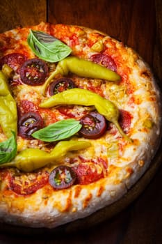 Homemade pizza with dried tomatoes, hot peppers and basil