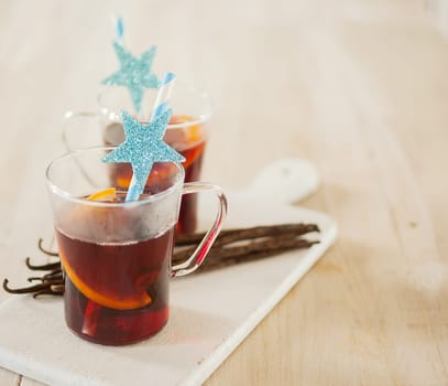Glass of festive hot Christmas gluhwein made from spiced mulled red wine seasoned with orange served with decorated star straws and vanilla pods on a white platter