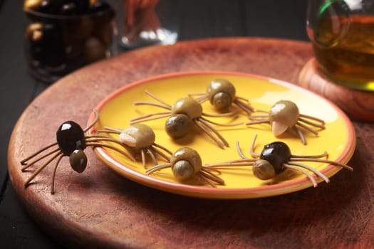 Creepy crawly edible Halloween spiders made from cured green and black olives with Italian spaghetti legs on a side table at a Halloween party for appetizers or favors for trick-ot-treating