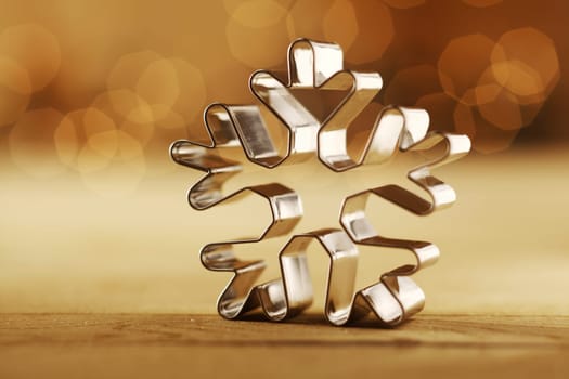 Snowflake Christmas background with a shiny aluminium cookie cutter standing upright on a sepia background with a faint bokeh of party lights and copyspace for your seasonal greeting