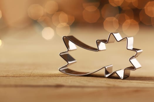 Decorative shiny metallic shooting star Christmas cookie cutter against a sepia colored background with a bokeh of twinkling party lights and copyspace for your Xmas or Advent greeting