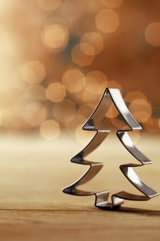 Shiny silver metallic Christmas tree cookie cutter decoration standing upright aginst a sepia background with a bokeh of sparkling party lights
