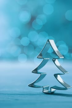Christmas tree cookie cutter decoration on a cool winter blue background with a feint bokeh of party lights and copyspace for your Xmas greeting