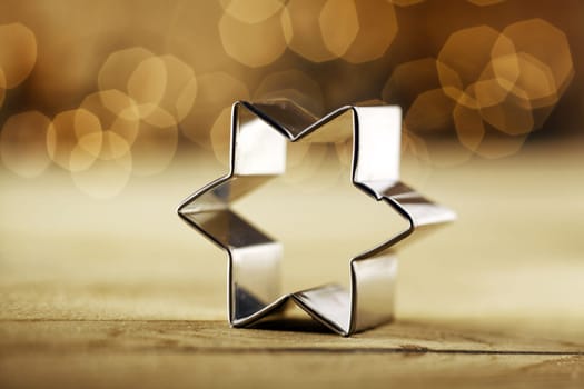 Close-up of a metallic star baking shape on a table with Christmas blurred glowing lights in the background