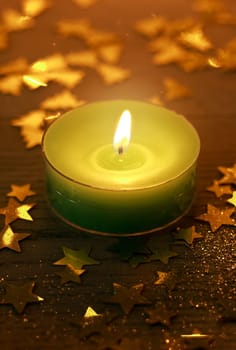 Green Christmas candle burning with glowing light surrounded by small golden decorative star shapes, high-angle close-up