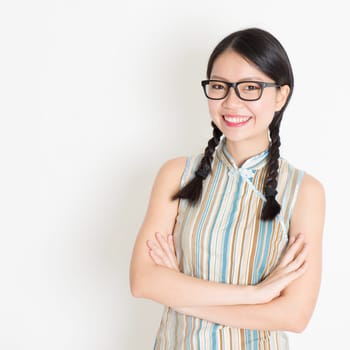 Portrait of beautiful Asian Chinese female smiling and looking at camera, in old-fashioned style cheongsam, standing on plain background.