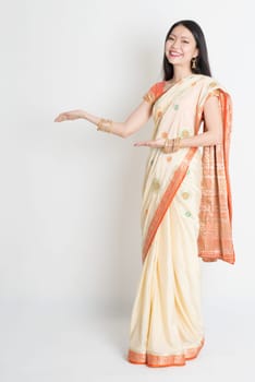 Full length Asian Indian girl hands showing something on plain background.