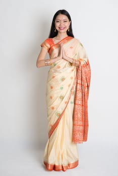 Asian Indian girl in a greeting pose, traditional sari costume, full length standing on plain background