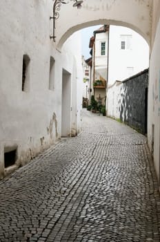 View into a small alley with arched element above and white plastered house walls and cobblestones in the city of Merano/South Tyrol