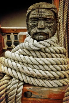 Head shaped wooden cleat on an old sailboat with ropes loop around it