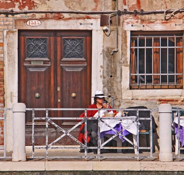 Every day life in Venice, woman with straw hat seats outside and drinks leisurely a glass of white wine