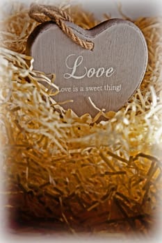 single brown wooden love heart in a love nest made of straw inscribed  love is a sweet thing