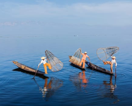 Myanmar travel attraction landmark - Traditional Burmese fishermen balancing with fishing net on boats at Inle lake in Myanmar famous for their distinctive one legged rowing style