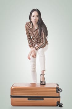 Modern Asian woman stand on a luggage, full length portrait on white background.