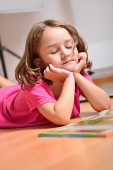 Little happy cute girl dreaming while reading a book