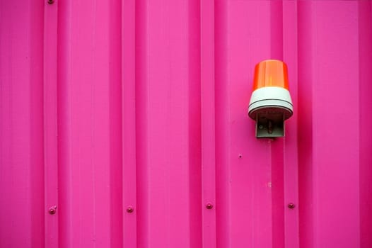 The photograph of a yellow warning light on an intensely coloured corrugated iron wall.