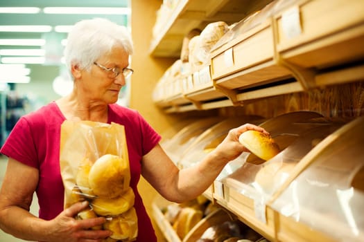Senior woman packing buns at supermarket