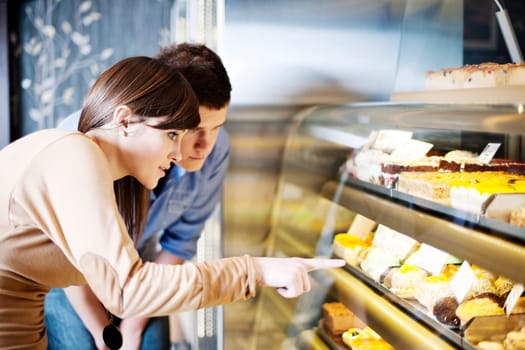 Young woman pointing on cakes in confectionery