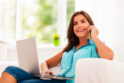Happy woman paying using laptop and talking on mobile phone