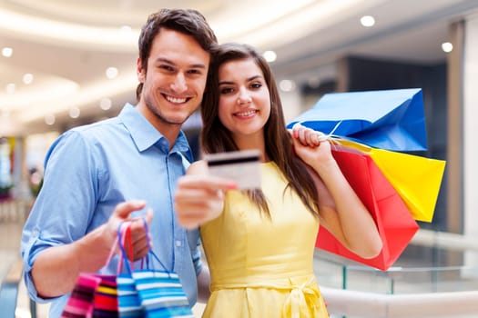 Beautiful couple showing credit card in the shopping mall