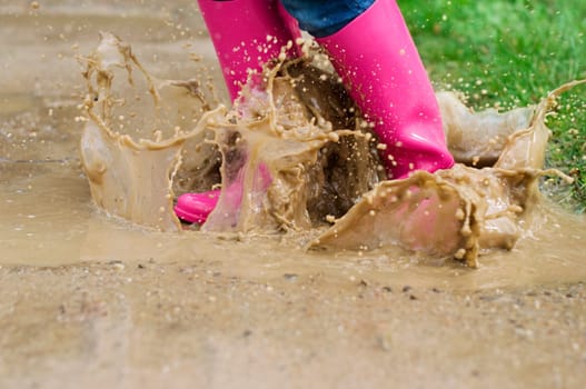 Young woman with rubber boots jumping in puddle