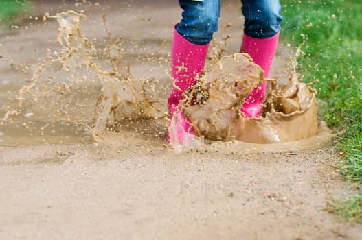 Young woman with rubber boots jumping in puddle