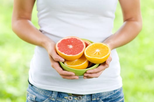 Young woman holding bowl filled oranges and grapefruits