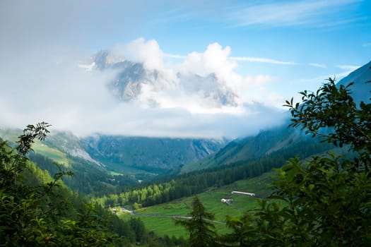 Valley in Les Ars Dessus, Switzerland, with forest and La Tsarve mountain surrounded by clouds in the background.
