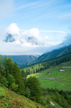Valley in Les Ars Dessus, Switzerland, with forest and La Tsarve mountain surrounded by clouds in the background.