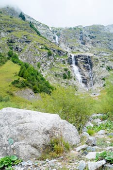 Natural cascade on hillside in La Fouly, Switzerland, and white bolder in the foreground.
